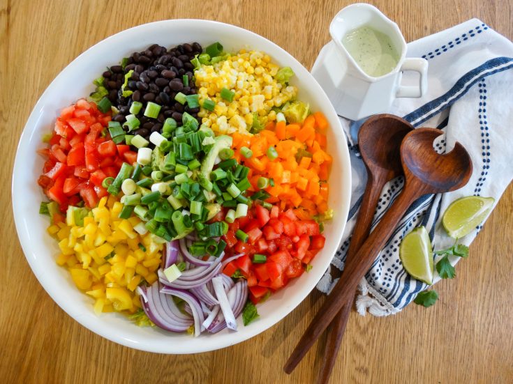 Southwest salad with veggies in salad bowl next to cilantro lime dressing in a pitcher